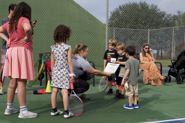 Coach handing certificates to young tennis players beside the court