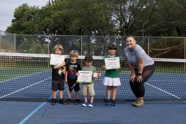 Five young players holding their certificates at the net with their coach