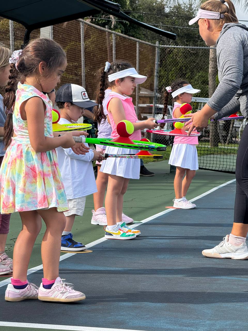 Preschool players balancing balls on their rackets as the coach watches