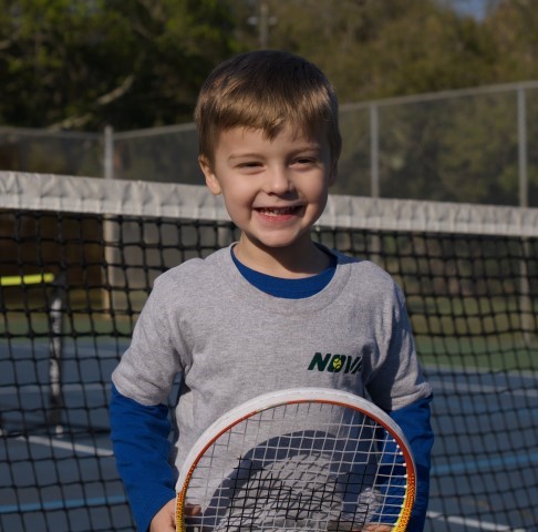 Smiling boy in a NOVA T-shirt holding his tennis racket