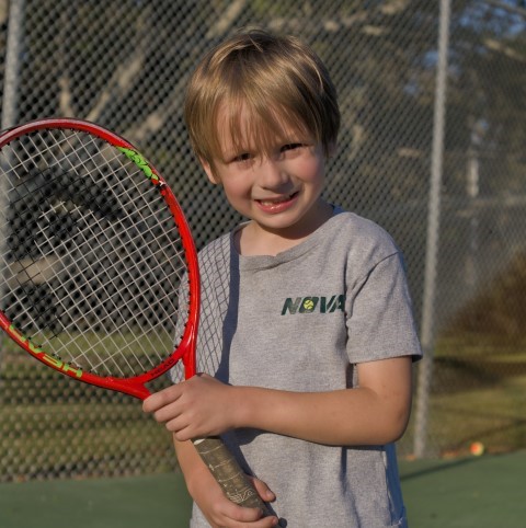 Boy with a red junior racket smiling on court