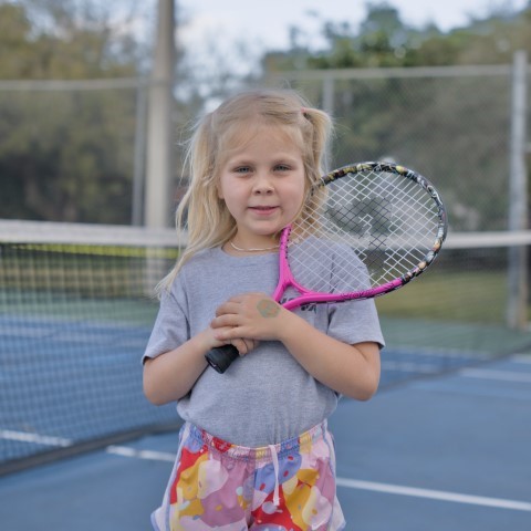 Little girl holding a pink racket on a blue hard court