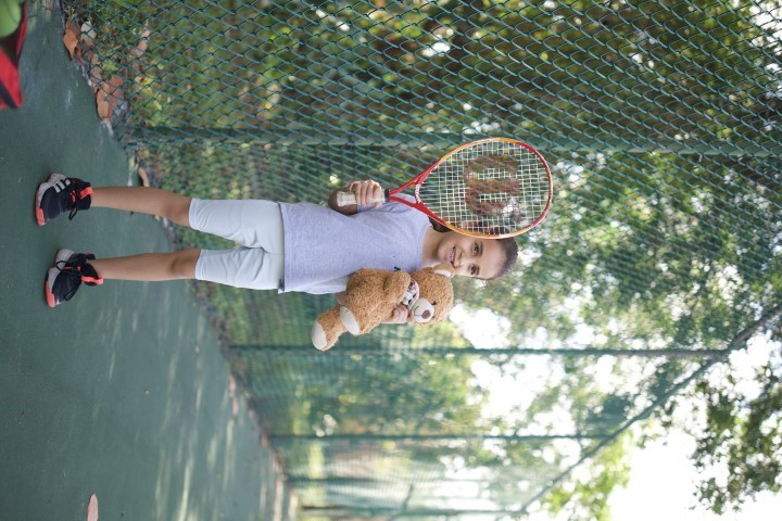 Girl with a racket and a teddy bear on the court path
