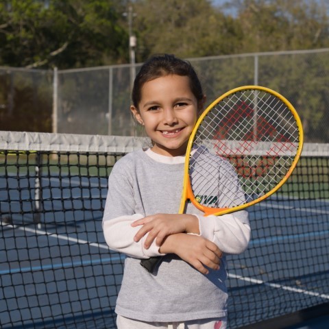 Girl with an orange racket smiling on court