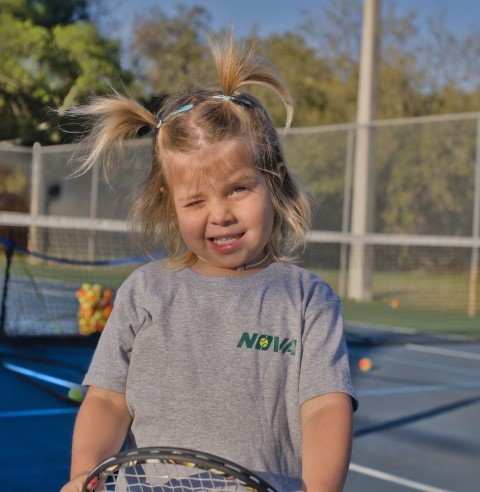 Young girl in a NOVA T-shirt squinting into the sun on court